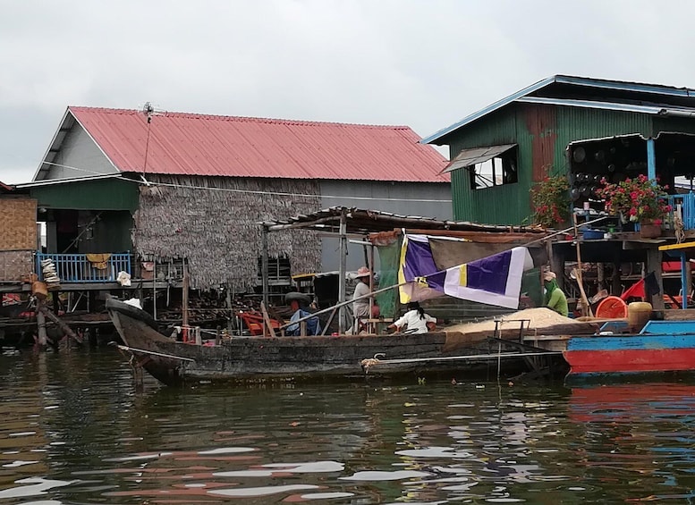 A traditional boat docked at a floating market with thatched-roof stalls and a flag. 1