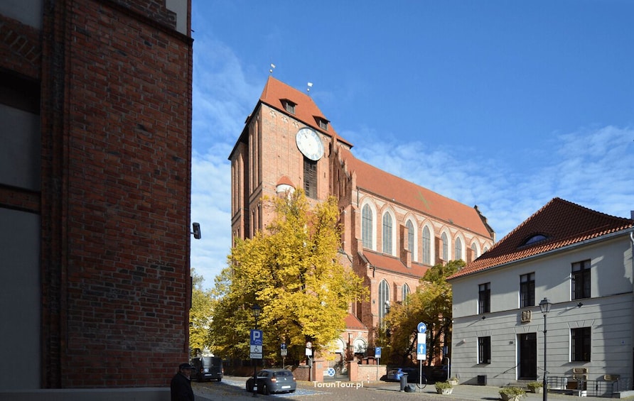 A historic church with a clock tower, surrounded by autumn trees and a white building with a red roof. 2