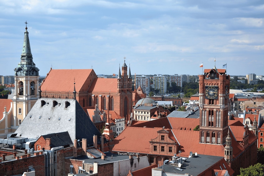 A historic cityscape with prominent red-roofed buildings, a church with a tall spire, and a clock tower. 5