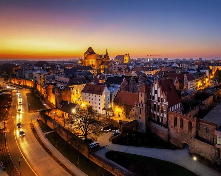 A cityscape at dusk with illuminated buildings and a prominent cathedral. 3