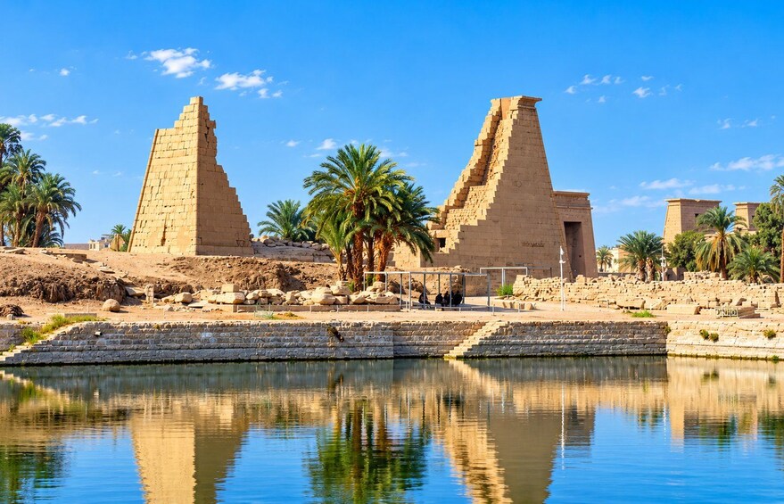 Ancient Egyptian pyramids, palm trees, and a calm river reflecting the structures. 2