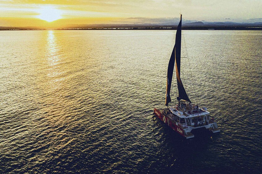 A sailboat on calm water during sunset with a distant shoreline and mountains. 3
