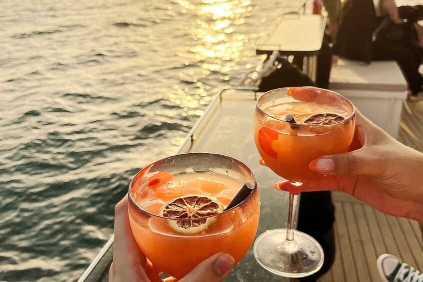 Two people holding glasses of a drink with a slice of dried fruit, on a boat with water in the background. 5