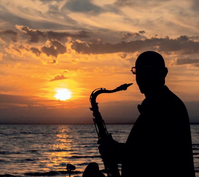 A silhouette of a person playing a saxophone against a sunset over the ocean. 1