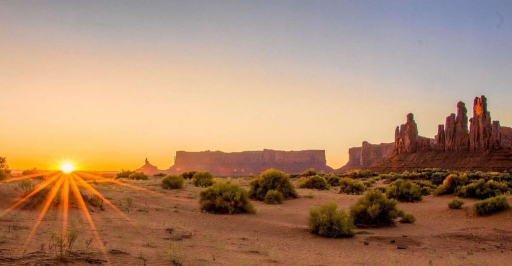A desert landscape with a sunset, sparse vegetation, and distinctive rock formations. 1