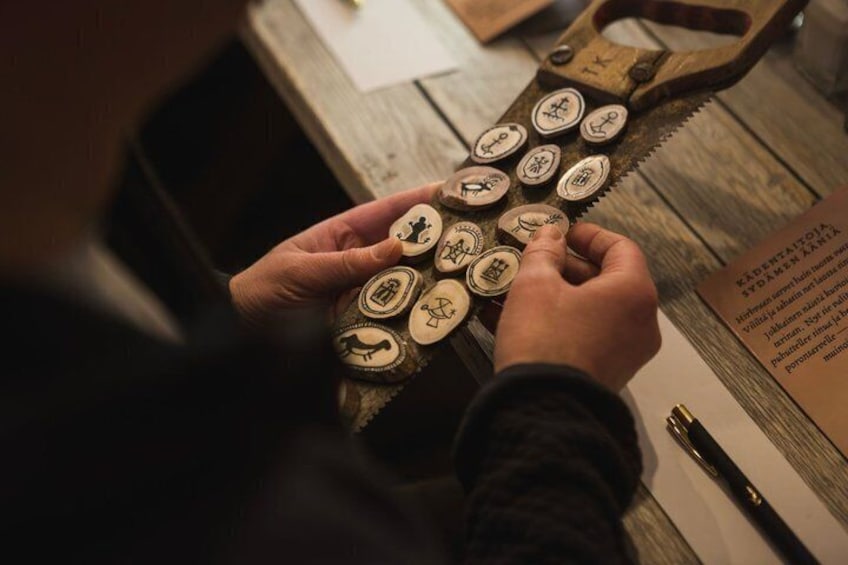 Hands holding a set of engraved metal stamps, a wooden saw, and a piece of paper with text. 5
