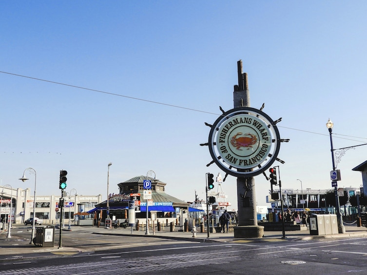 Une intersection où se croisent deux rues, avec un grand panneau circulaire bien visible, orné d’un emblème représentant un crabe et de l’inscription « OF FISHERMAN’S WHARF SAN FRANCISCO ». 4