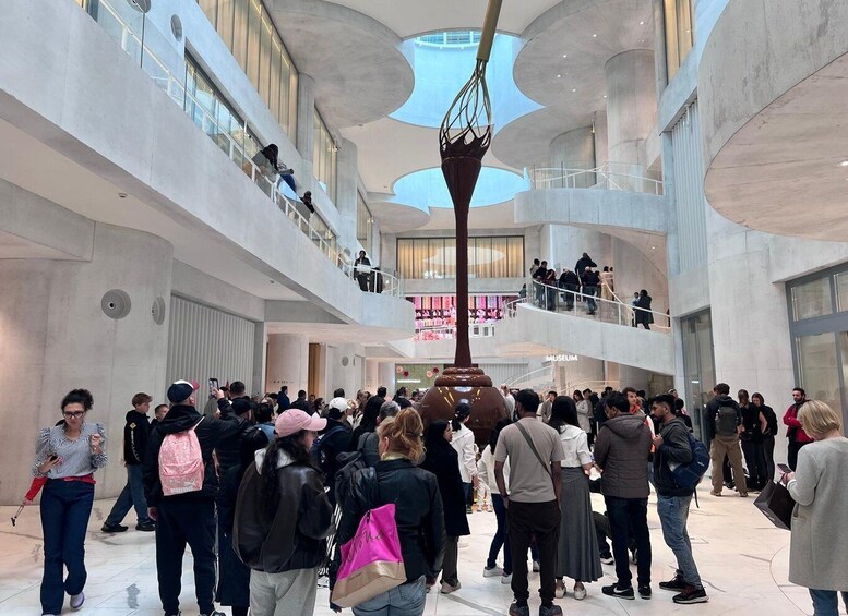 A modern building interior with a central sculpture, glass railings, and a crowd of people. 5