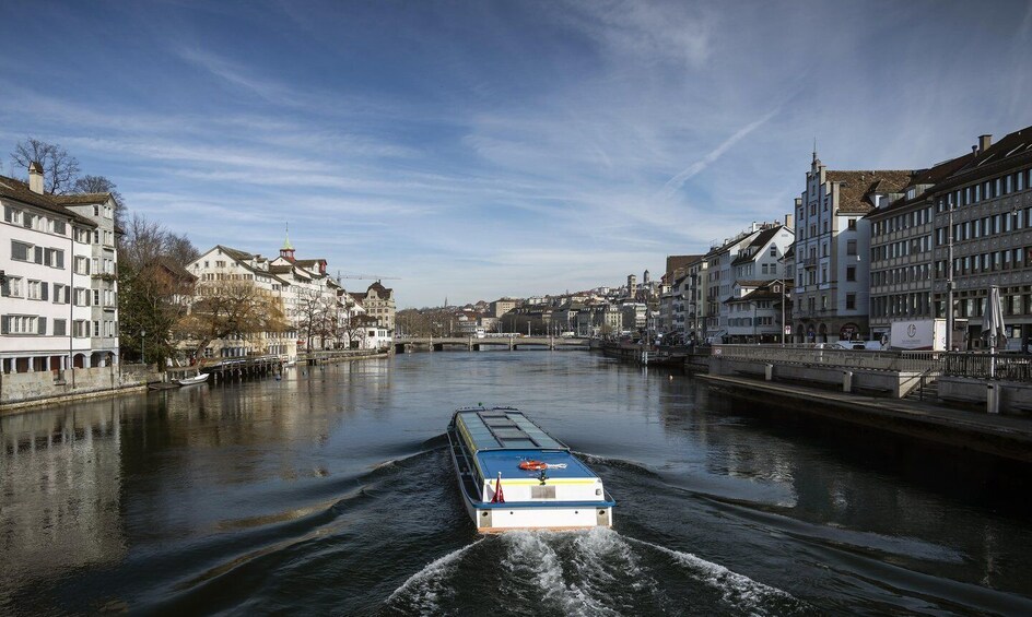 A river with a boat moving through it, surrounded by buildings and a bridge in the background. 3