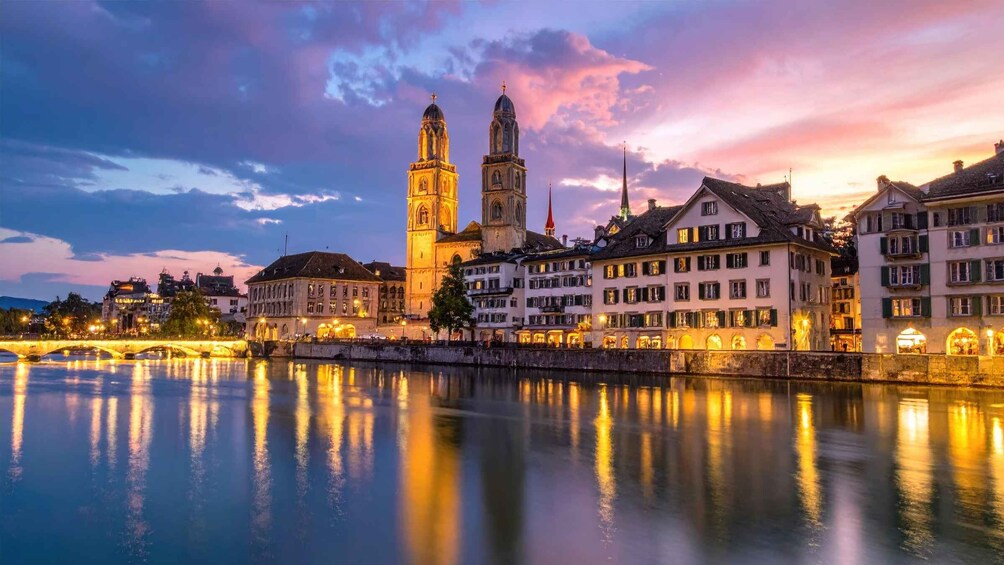 A riverside cityscape with illuminated buildings and a prominent tower at dusk. 2
