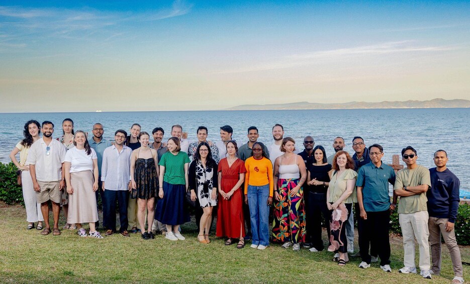 A group of people standing on grass by a body of water with a distant shoreline. 2