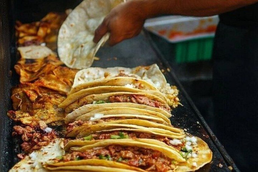 A stack of tacos on a grill with a tortilla being lifted. 2