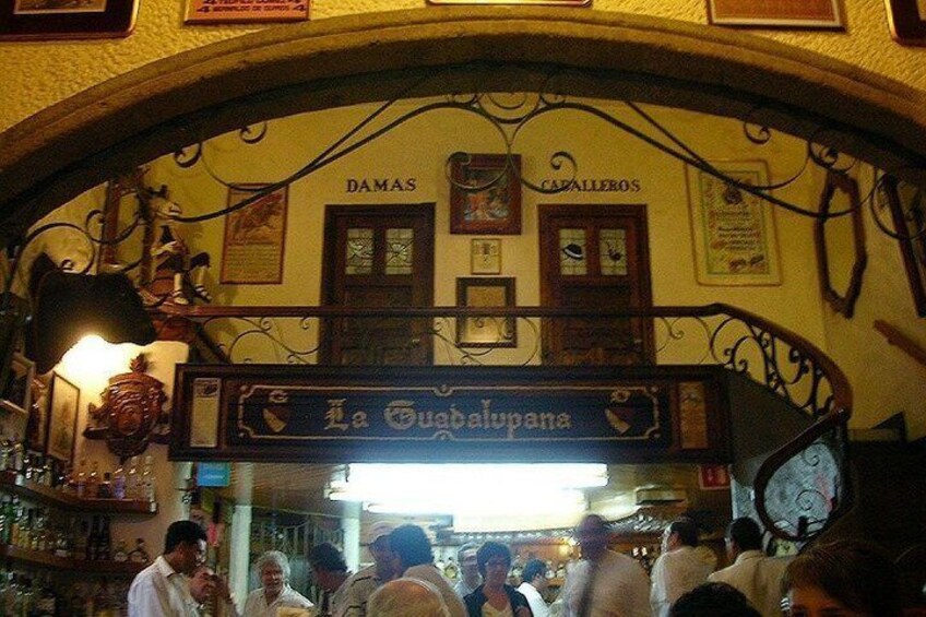 An indoor bar with a sign reading 'La Guabelupana' and 'DAMAS CAPALLEROS' above. 5