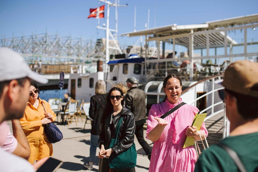 A group of people standing on a dock with boats and a flag in the background. 1