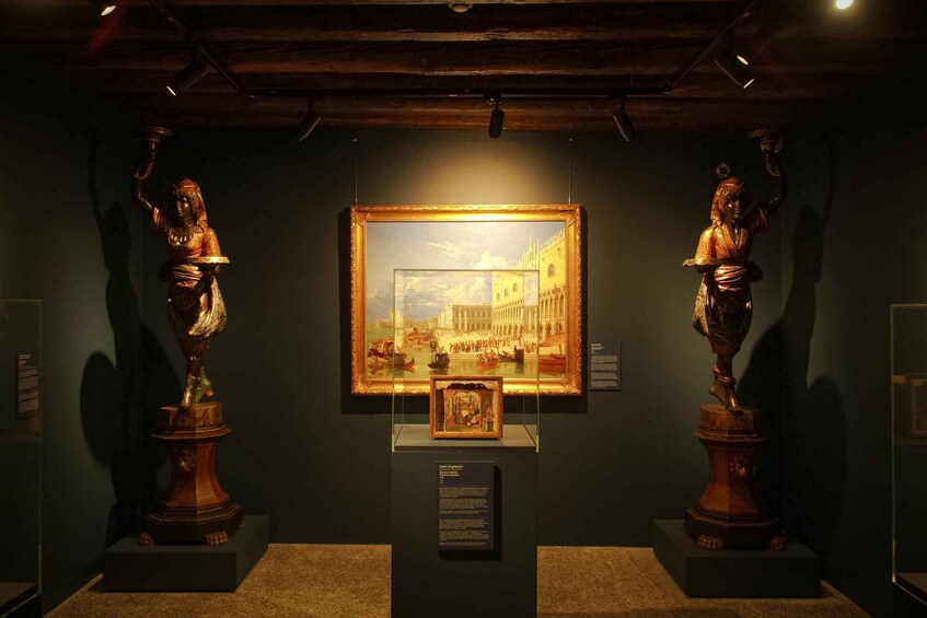 A museum exhibit with two wooden statues, a framed painting, and informational plaques. 5