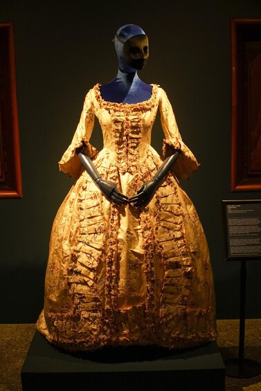 A mannequin in a detailed historical dress with lace and floral patterns, displayed in a museum setting. 4