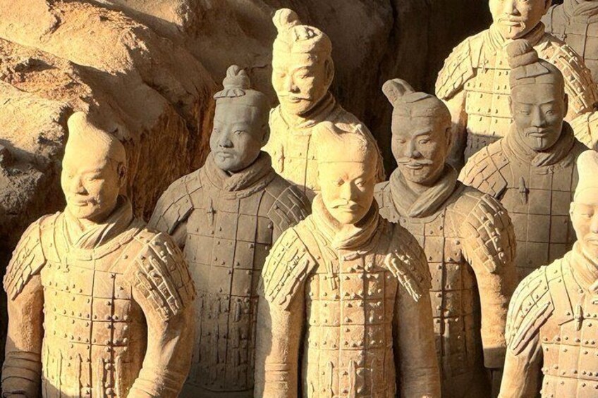 Terracottasoldaten in uniform, opgesteld in formatie, met een rotsachtige achtergrond. 3