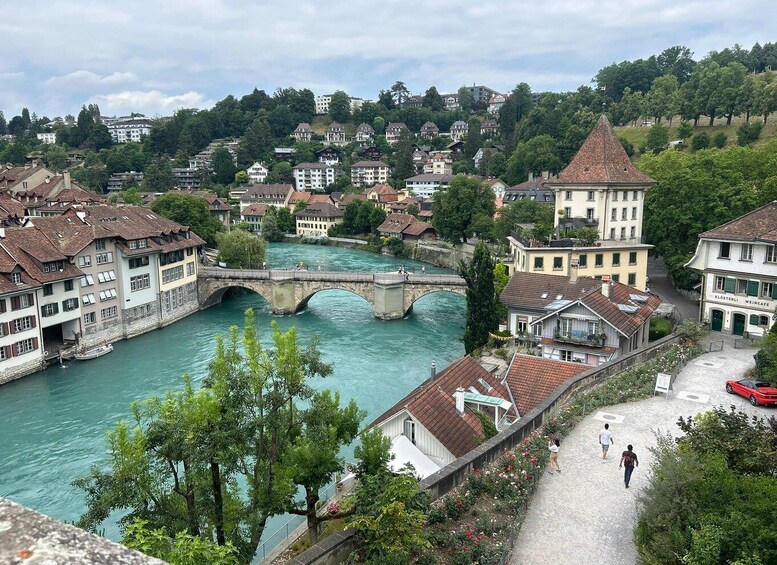 A river with a stone bridge, buildings, and a hill with trees in the background. 4