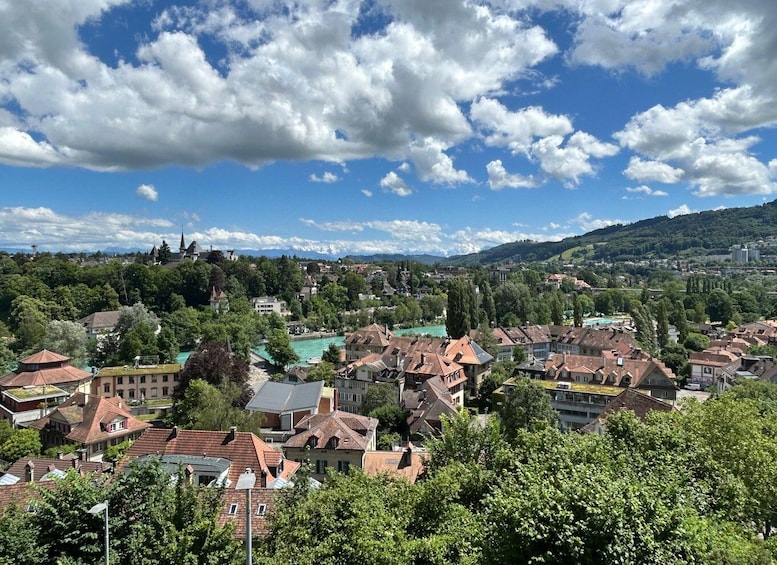 A town with red-roofed houses, a river, and mountains in the background. 1