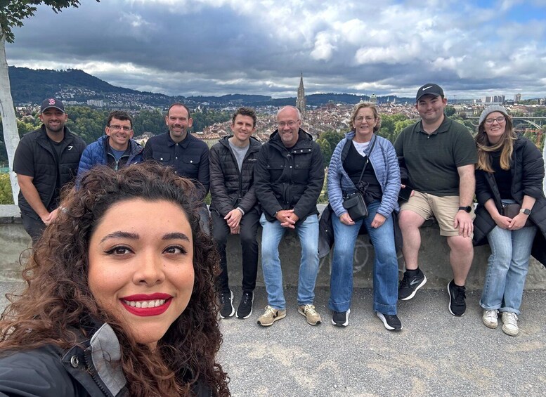 A group of people sitting on a ledge overlooking a cityscape with a prominent church spire. 2