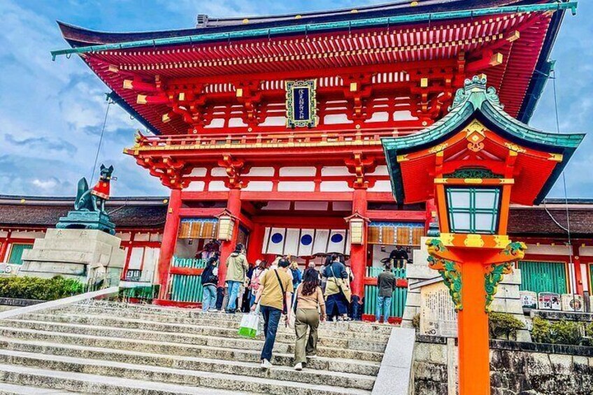 Un temple japonais traditionnel, avec une architecture aux couleurs rouge et verte, une statue et des visiteurs montant les marches. 1