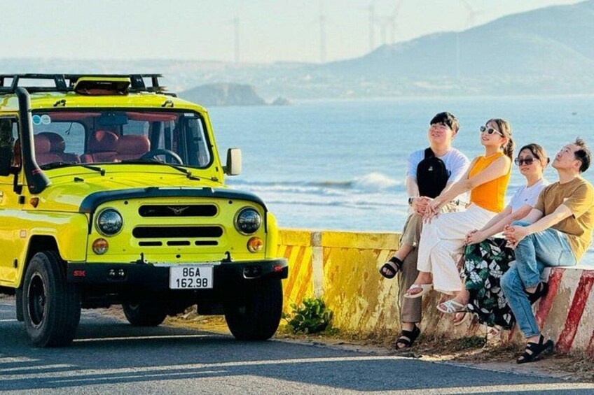 A yellow vehicle parked by the roadside with a bridge and water in the background. 4