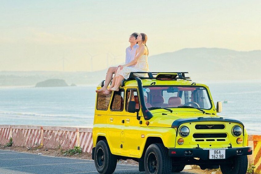 A yellow vehicle parked by the seaside with a couple on top. 1