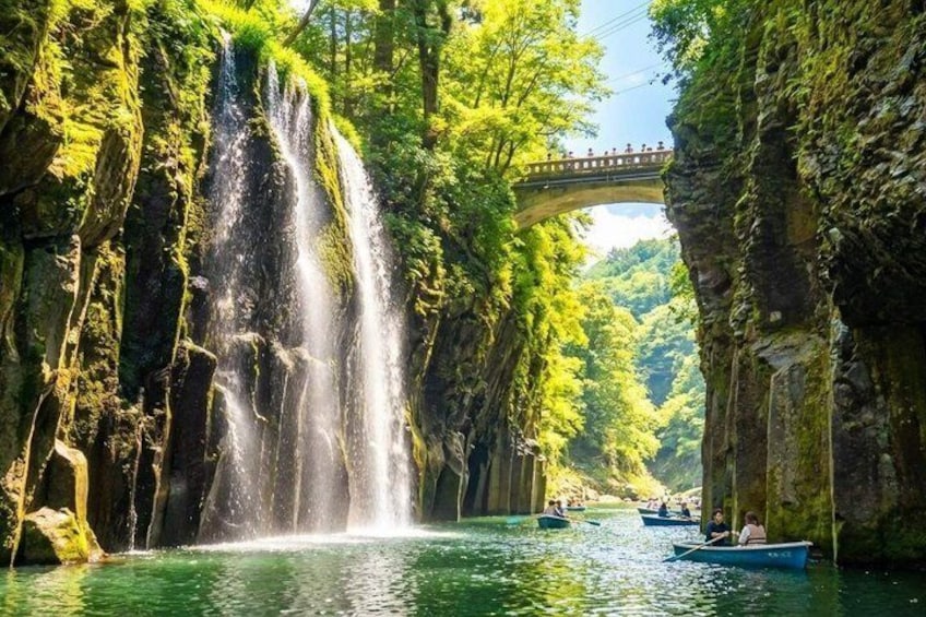 Una cascada, un puente y barcos en un río rodeado de vegetación. 1