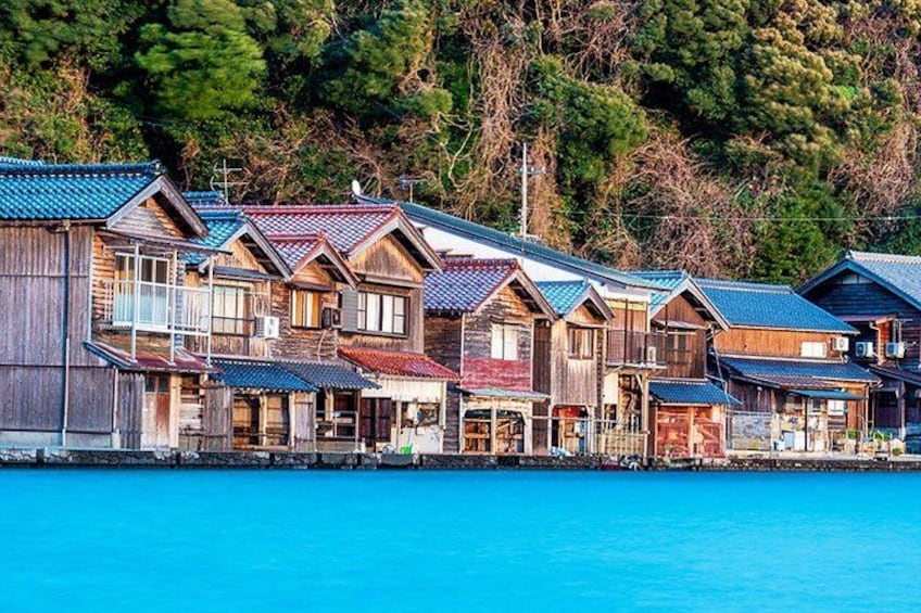 A row of wooden houses with blue roofs by a turquoise sea. 2