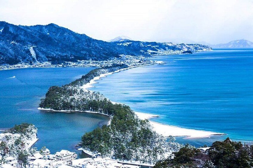 A coastal landscape with a curving bay, snow-covered trees, and distant mountains. 5