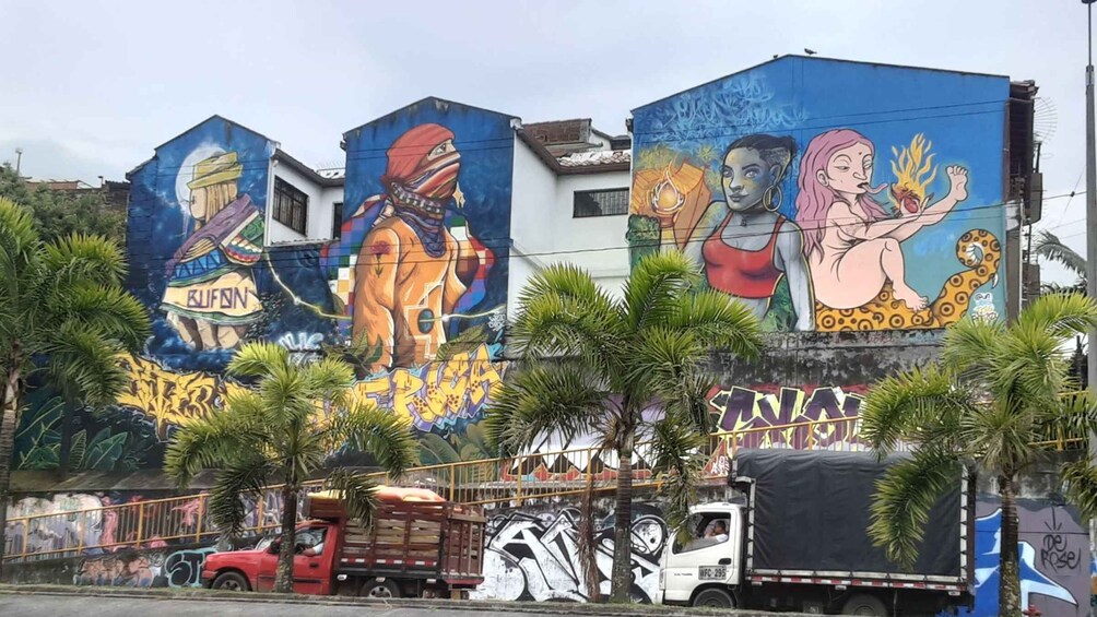 A building with colorful murals, palm trees, and parked trucks. 1