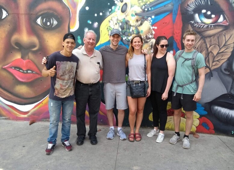 A group of people standing in front of a colorful mural with abstract designs and a prominent eye. 4