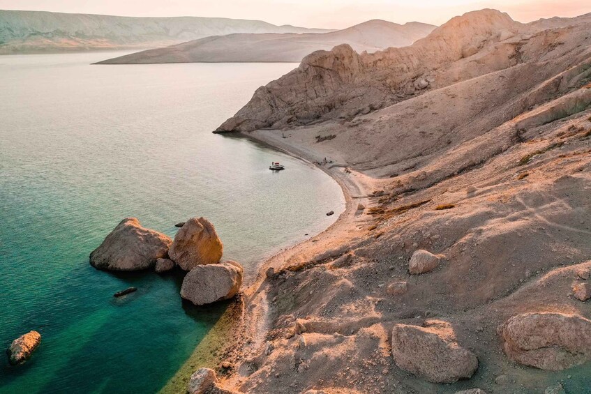 A coastal landscape with a clear blue sea, rocky terrain, and a boat on the water. 1
