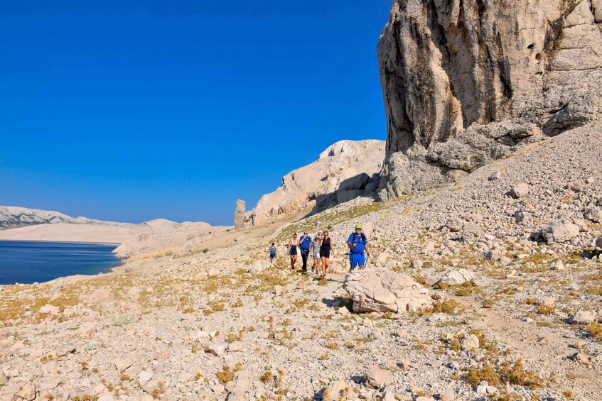 A rocky terrain with a group of hikers and a large cliff by a body of water. 5