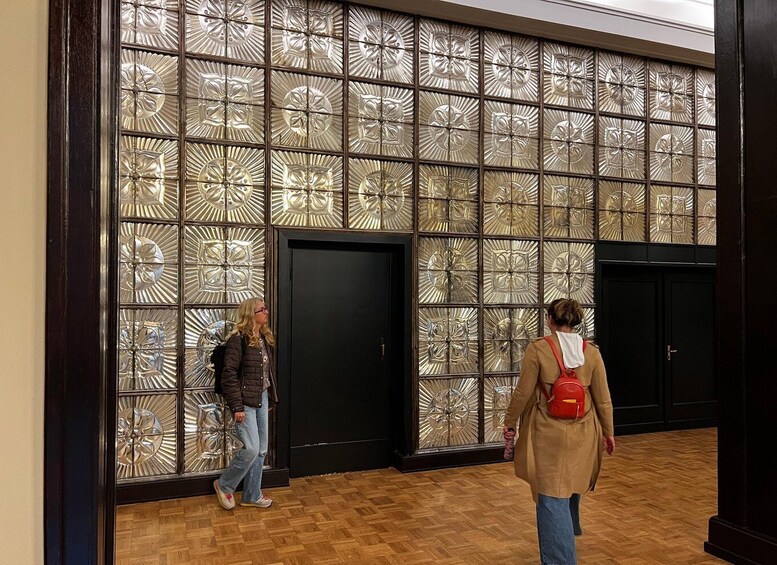 Two people walking past a wall with a geometric pattern. 2