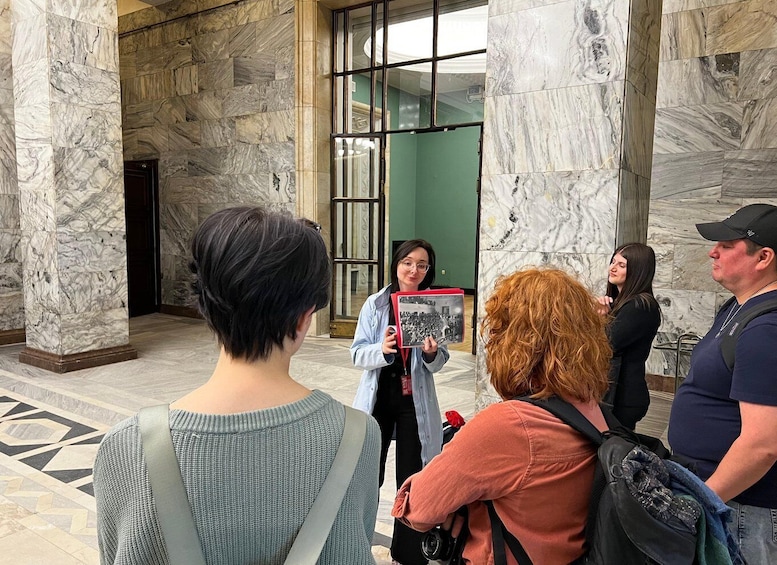 A group of people in a marble-floored lobby with a glass door and a green wall. 5