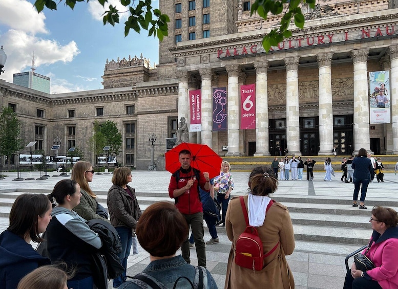 A group of people standing in front of a large building with classical architecture, banners, and a clear sky. 4