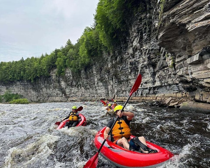 Two people kayaking on a river with rocky cliffs in the background. 1