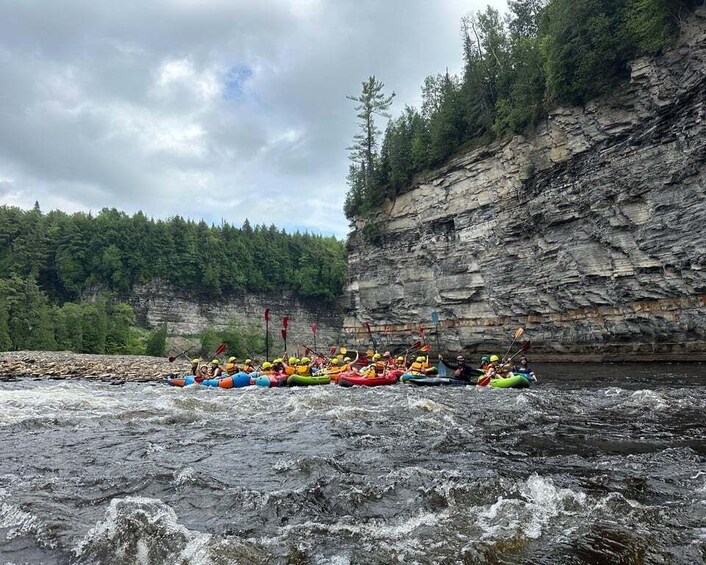 A group of kayakers navigating a river with a rocky cliff in the background. 5
