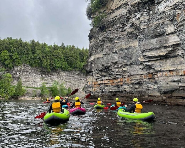 A group of kayakers navigating a river with a rocky cliff in the background. 2