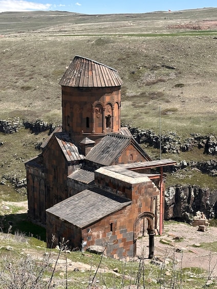 An ancient stone church with a bell tower, surrounded by a rocky landscape and sparse vegetation. 1