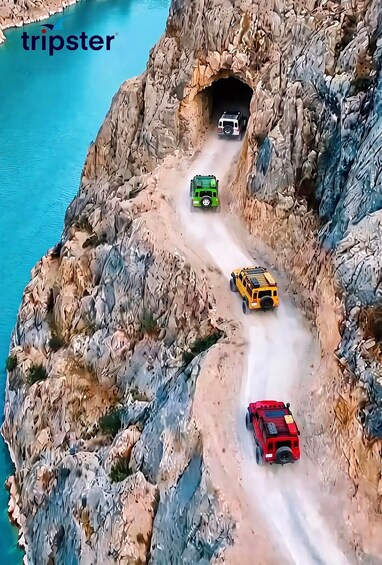 A rocky terrain with a tunnel entrance and four toy cars navigating a narrow path. 2