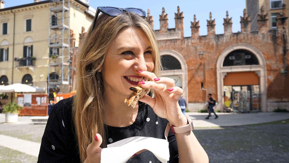A person eating a slice of pizza outdoors with a historic building in the background. 1