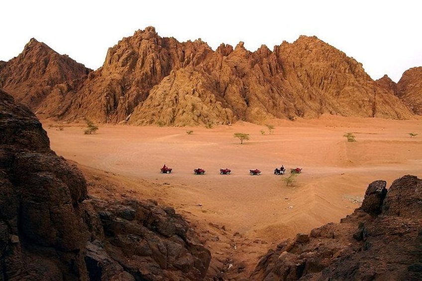 A desert landscape with rocky mountains and a group of off-road vehicles. 4
