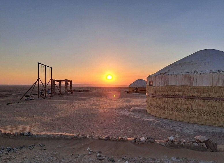 A desert landscape with yurts and a traditional structure at sunset. 1