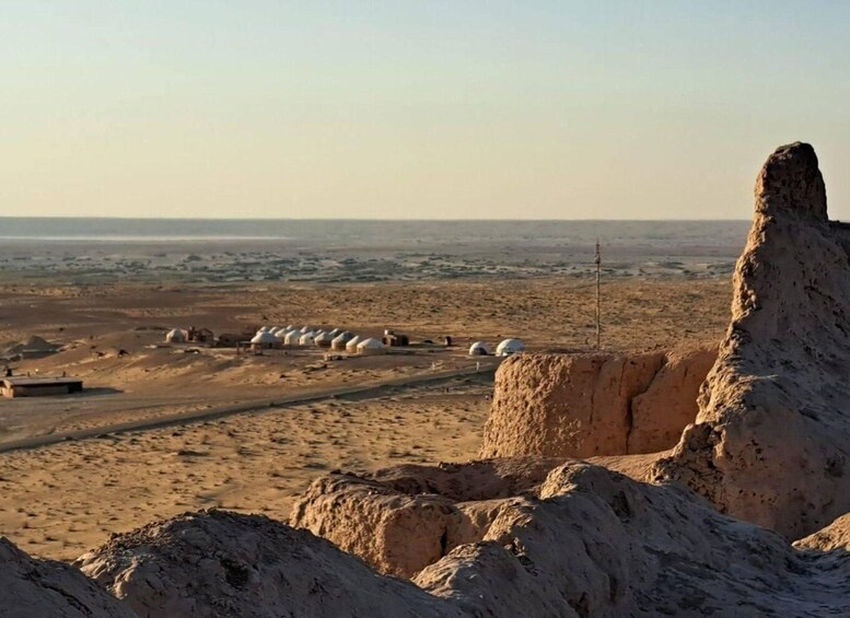 A desert landscape with white yurts and a prominent rock formation. 2