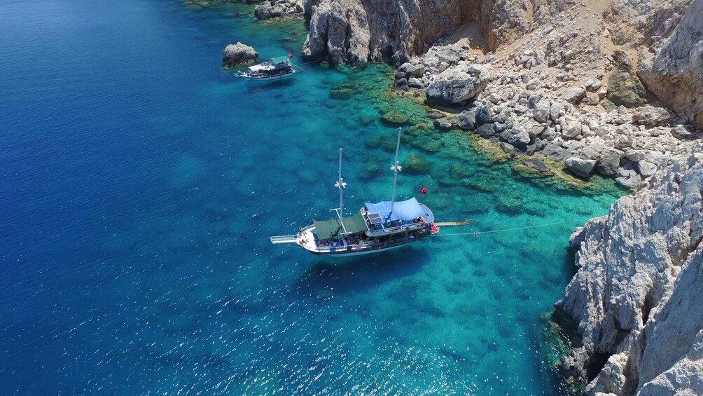 A boat anchored near rocky cliffs in clear blue waters. 2