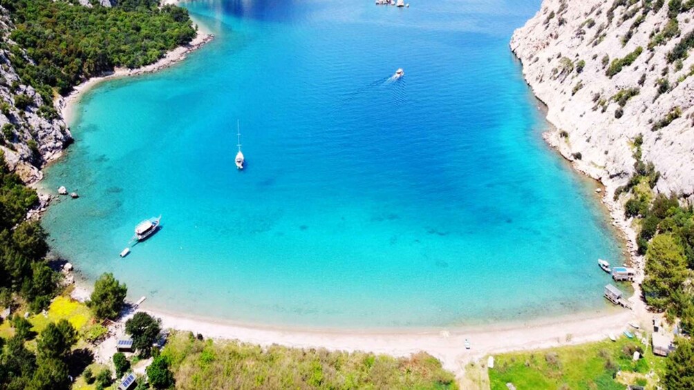 A turquoise bay with boats, a sandy beach, and rocky cliffs. 5