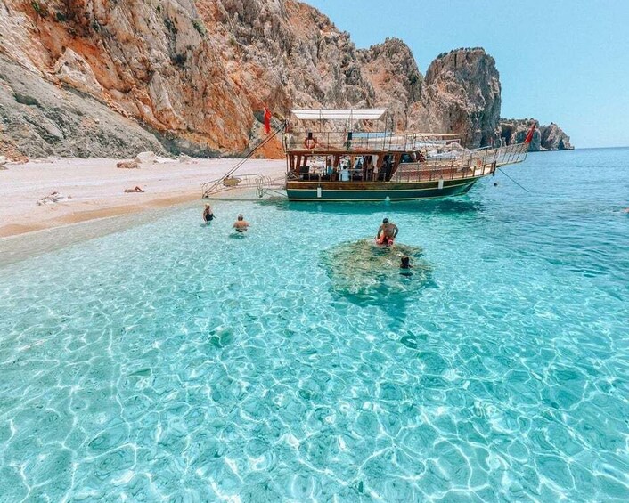 A boat on a clear turquoise sea with rocky cliffs in the background. 4