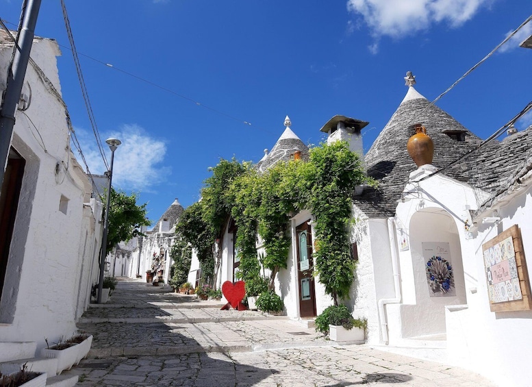 A narrow cobblestone street lined with white buildings featuring conical roofs and ivy. 1